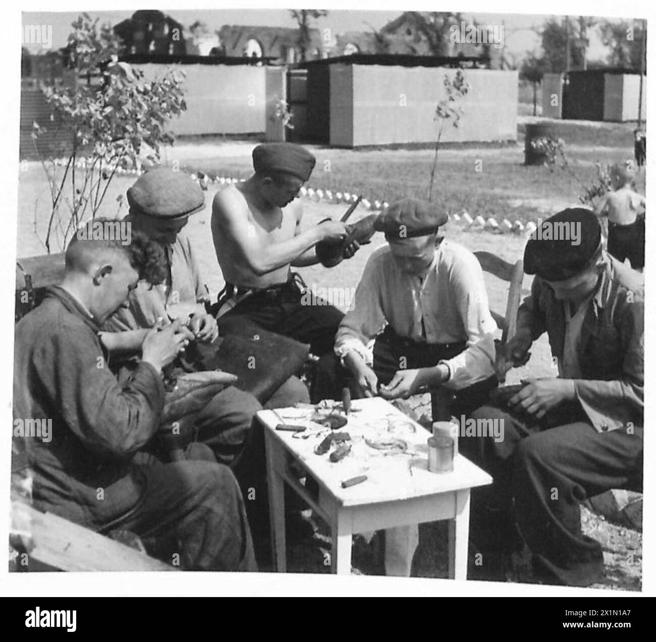 In un campo di sfollati russi, un ciabattino ripara scarpe per altri residenti usando pelle britannica, sotto la gestione dell'esercito britannico, 21st Army Group. Foto Stock