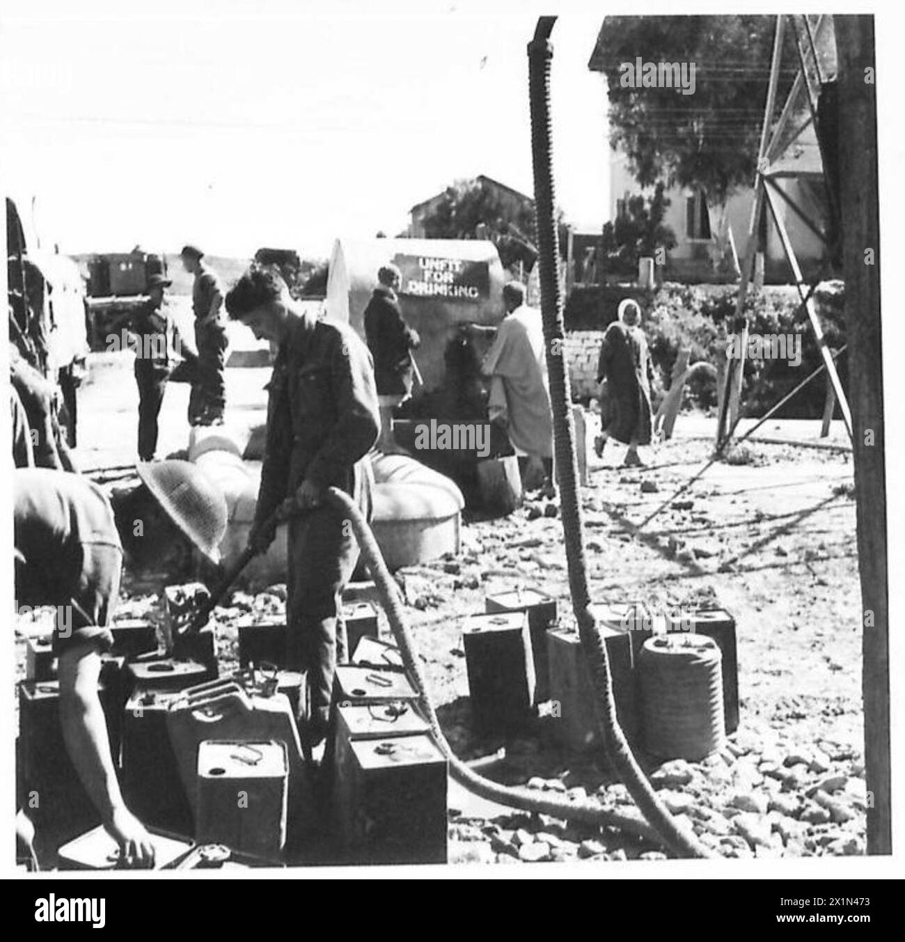 I soldati riempiono le lattine d'acqua per la prima armata, mentre la gente locale raccoglie l'acqua da un ben etichettato "non adatto a bere", evidenziando le pratiche di approvvigionamento idrico dell'esercito britannico. Foto Stock