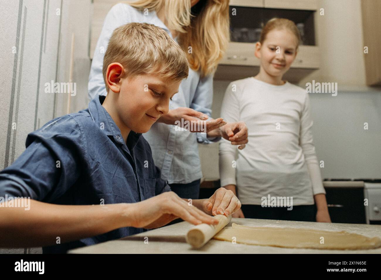 Diversi individui sono in piedi intorno a una cucina, impegnati a preparare il cibo insieme. Vengono visti coordinare, tritare gli ingredienti, cucinare, e. Foto Stock