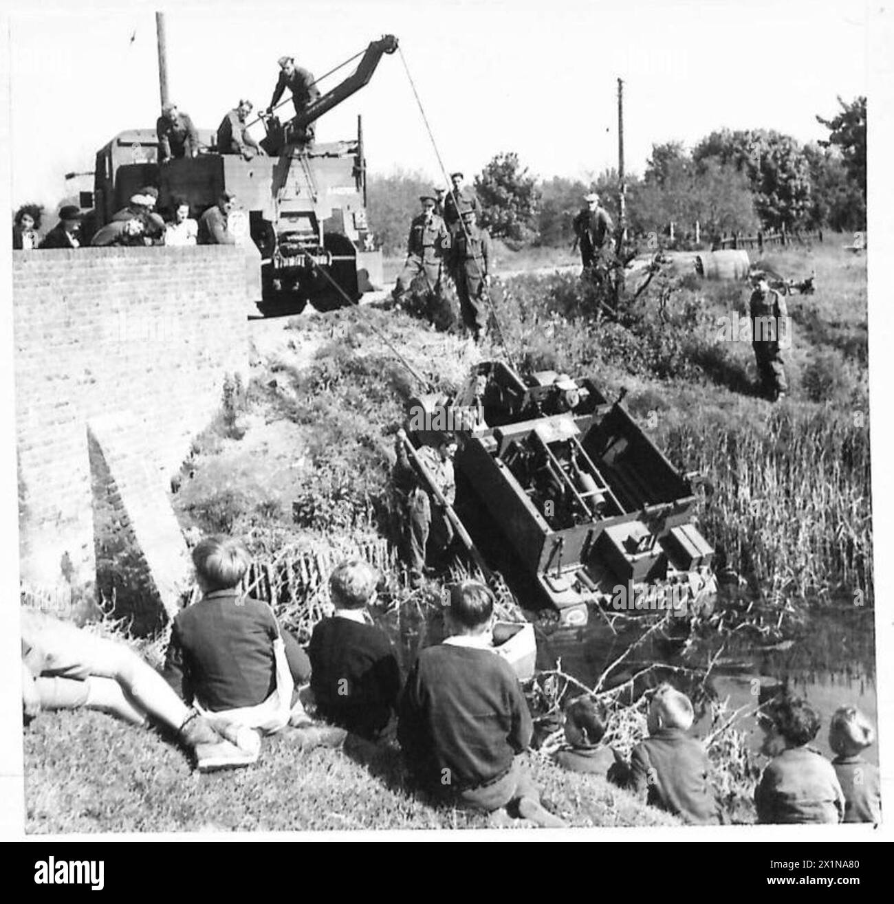 La sezione di recupero del R.A.O.C. trasporta un vettore Bren da un ruscello lungo la strada, mentre gli scolari guardano dalla banca, British Army. Foto Stock