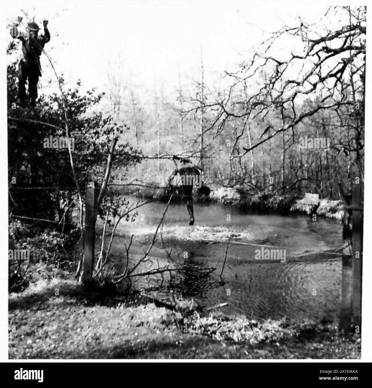 SCUOLA DI ADDESTRAMENTO DA BATTAGLIA - un uomo cade dal ponte di filo metallico su un fiume in 12 piedi di acqua, mentre un altro negozia l'attraversamento con maggiore cura, British Army Foto Stock