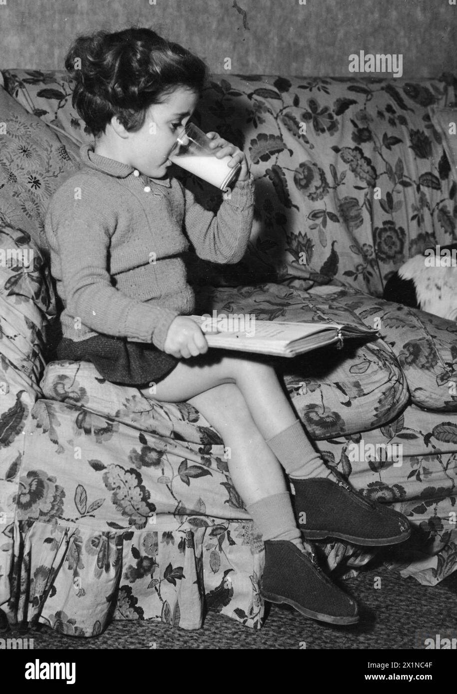 MINISTRY OF FOOD MEETALS, UK, c 1943 - Una ragazza beve un bicchiere di latte mentre si siede su un divano per leggere un libro. Il latte era considerato estremamente importante per la salute dei bambini, e la priorità per il latte fresco in tempo di guerra era data ai bambini: Gli adulti dovevano fare a meno del latte in polvere. Una copia in bianco e nero negativa , Foto Stock