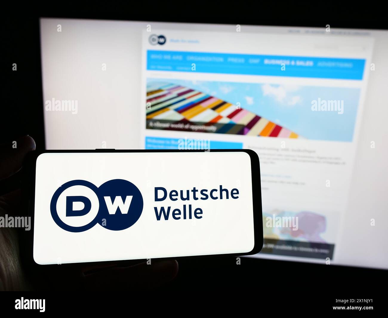 Persona che possiede uno smartphone con il logo dell'emittente statale tedesca Deutsche Welle (DW) davanti al sito web. Mettere a fuoco il display del telefono. Foto Stock
