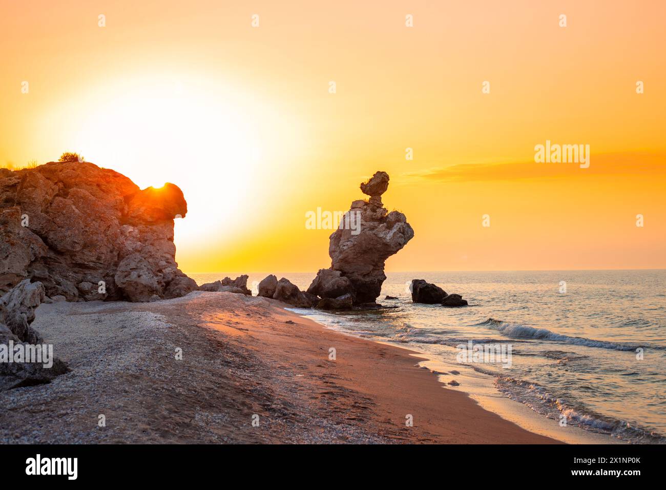 Paesaggio al tramonto. Un'elegante roccia di pietra a forma di gallo sulla riva del mare durante il tramonto. Vista sul mare. Foto Stock
