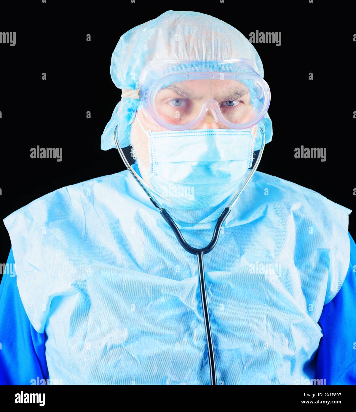 Primo piano ritratto di medico serio in maschera protettiva, occhiali e tappo chirurgico monouso con stetoscopio. Infermiere maschio in maschera chirurgica e. Foto Stock