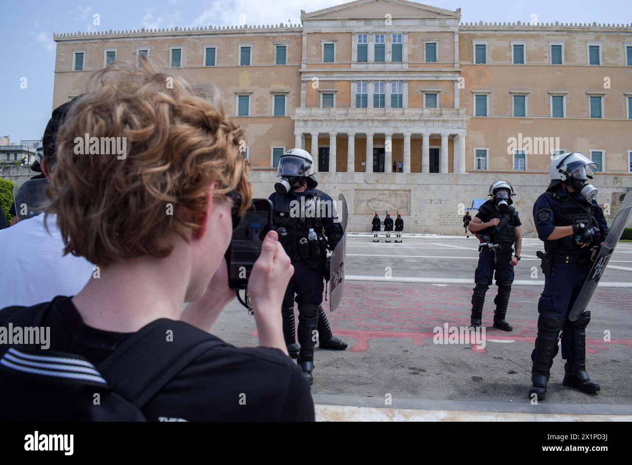 Atene, Grecia. 17 aprile 2024. I turisti insistono nel fare foto del cambio delle guardie in Piazza Syntagma nonostante la pesante presenza della polizia anti-sommossa a causa delle marce di protesta. Migliaia di persone sono scese per le strade della capitale greca durante uno sciopero nazionale di 24 ore che condannava la crescente povertà e l’inflazione che richiedeva aumenti salariali e il ripristino dei contratti collettivi di lavoro. Crediti: Dimitris Aspiotis/Alamy Live News Foto Stock