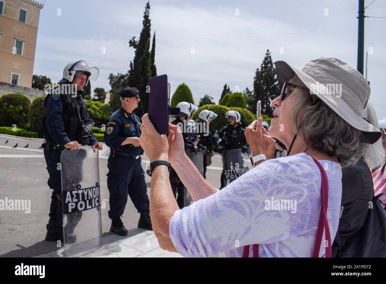 Atene, Grecia. 17 aprile 2024. I turisti insistono nel fare foto del cambio delle guardie in Piazza Syntagma nonostante la pesante presenza della polizia anti-sommossa a causa delle marce di protesta. Migliaia di persone sono scese per le strade della capitale greca durante uno sciopero nazionale di 24 ore che condannava la crescente povertà e l’inflazione che richiedeva aumenti salariali e il ripristino dei contratti collettivi di lavoro. Crediti: Dimitris Aspiotis/Alamy Live News Foto Stock