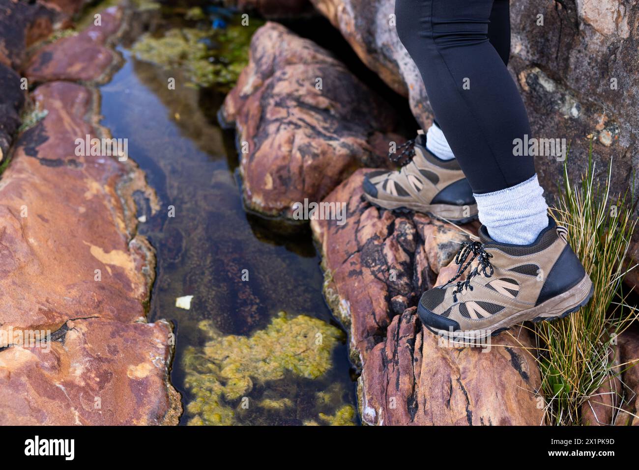 Escursionista femminile birazziale scalda sulle rocce dal ruscello, circondato da una vegetazione lussureggiante Foto Stock