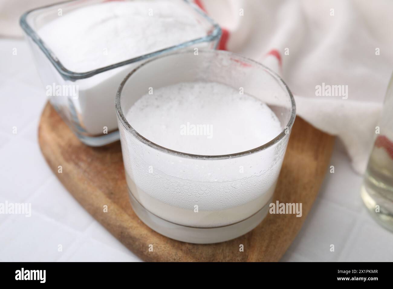 Reazione chimica dell'aceto e bicarbonato di sodio in un recipiente di vetro su un tavolo bianco, primo piano Foto Stock