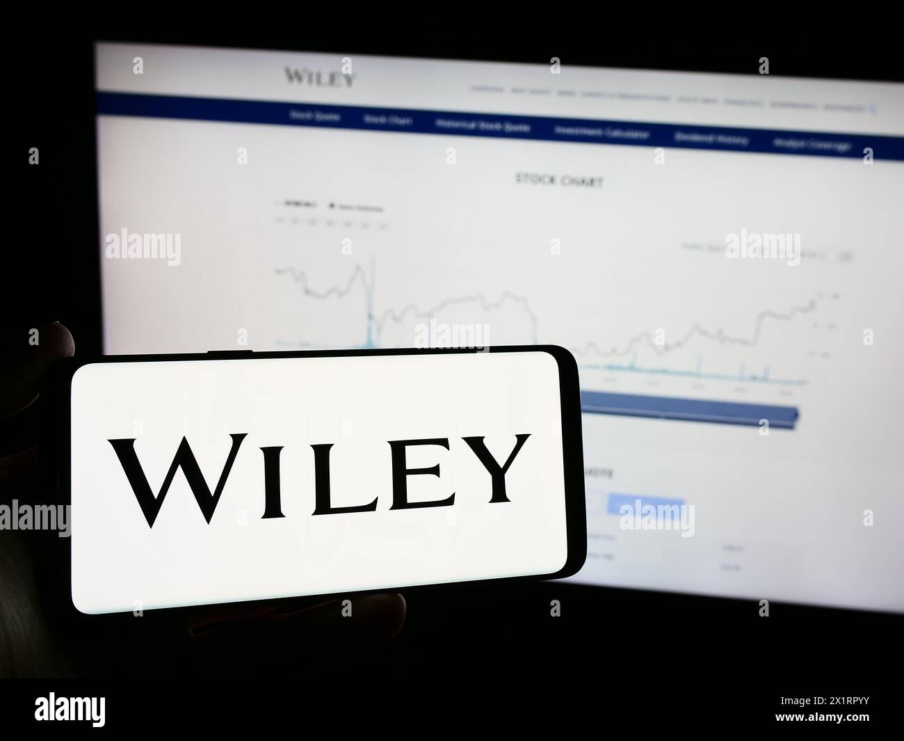 Persona che possiede un telefono cellulare con il logo della casa editrice americana John Wiley and Sons Inc. Davanti alla pagina Web. Mettere a fuoco il display del telefono. Foto Stock