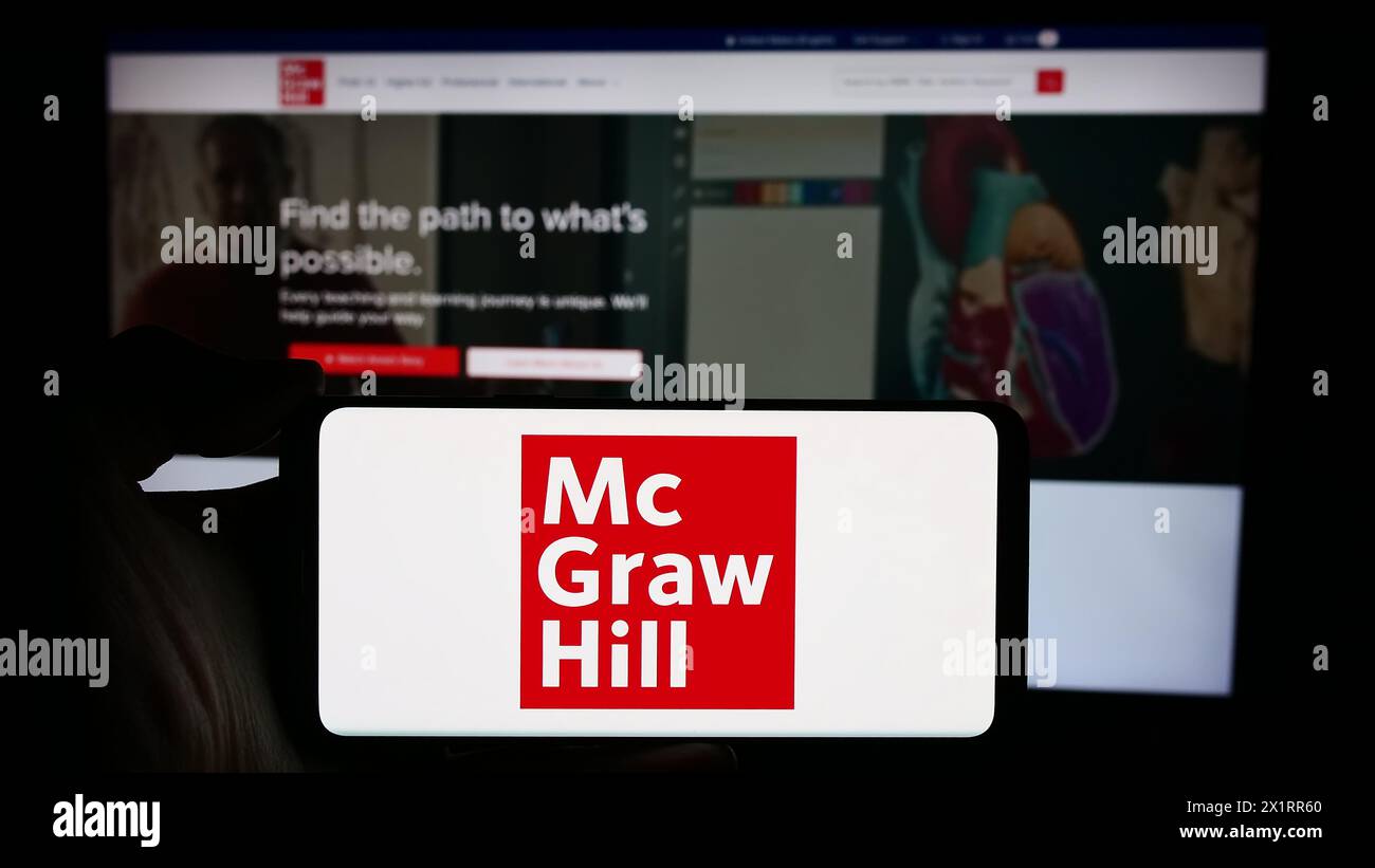 Persona che detiene un cellulare con il logo della casa editrice statunitense McGraw Hill LLC di fronte alla pagina Web aziendale. Mettere a fuoco il display del telefono. Foto Stock