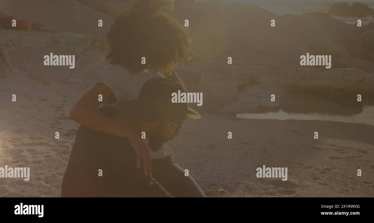 Afroamericano giovane adulto e birazziale giovane adulto seduto sulla spiaggia al tramonto Foto Stock