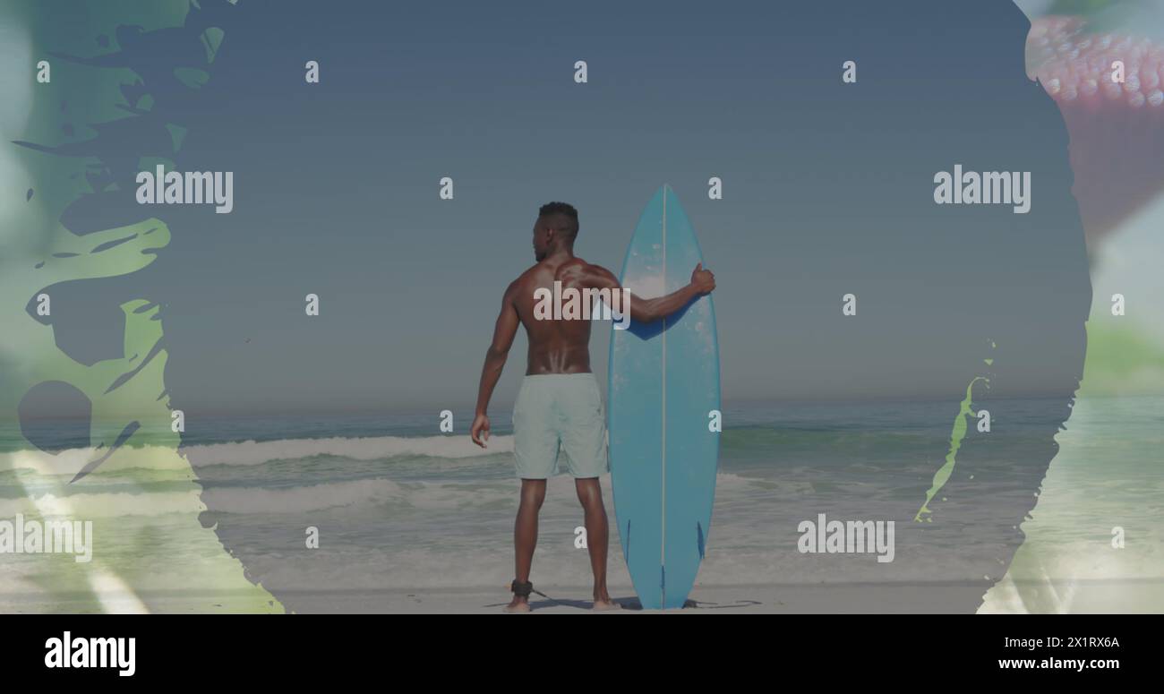 Uomo afroamericano che tiene una tavola da surf sulla spiaggia, guardando l'oceano Foto Stock