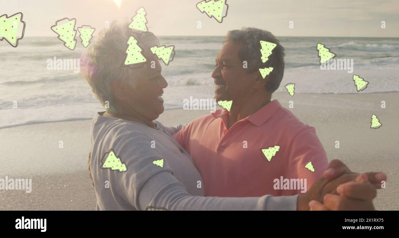 Coppia birazziale senior che balla sulla spiaggia, circondata da alberi di Natale Foto Stock