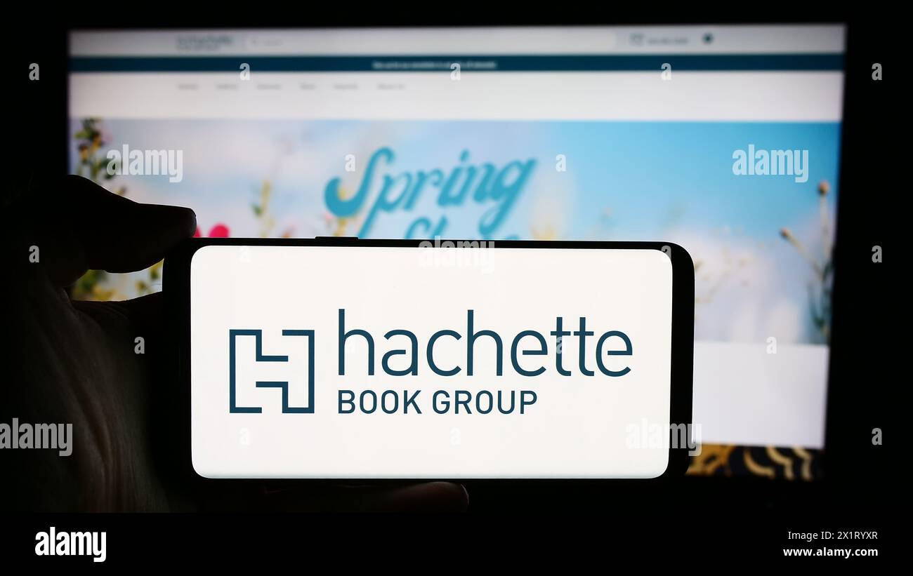 Persona che detiene un cellulare con il logo della casa editrice statunitense Hachette Book Group Inc (HBG) di fronte alla pagina Web aziendale. Mettere a fuoco il display del telefono. Foto Stock
