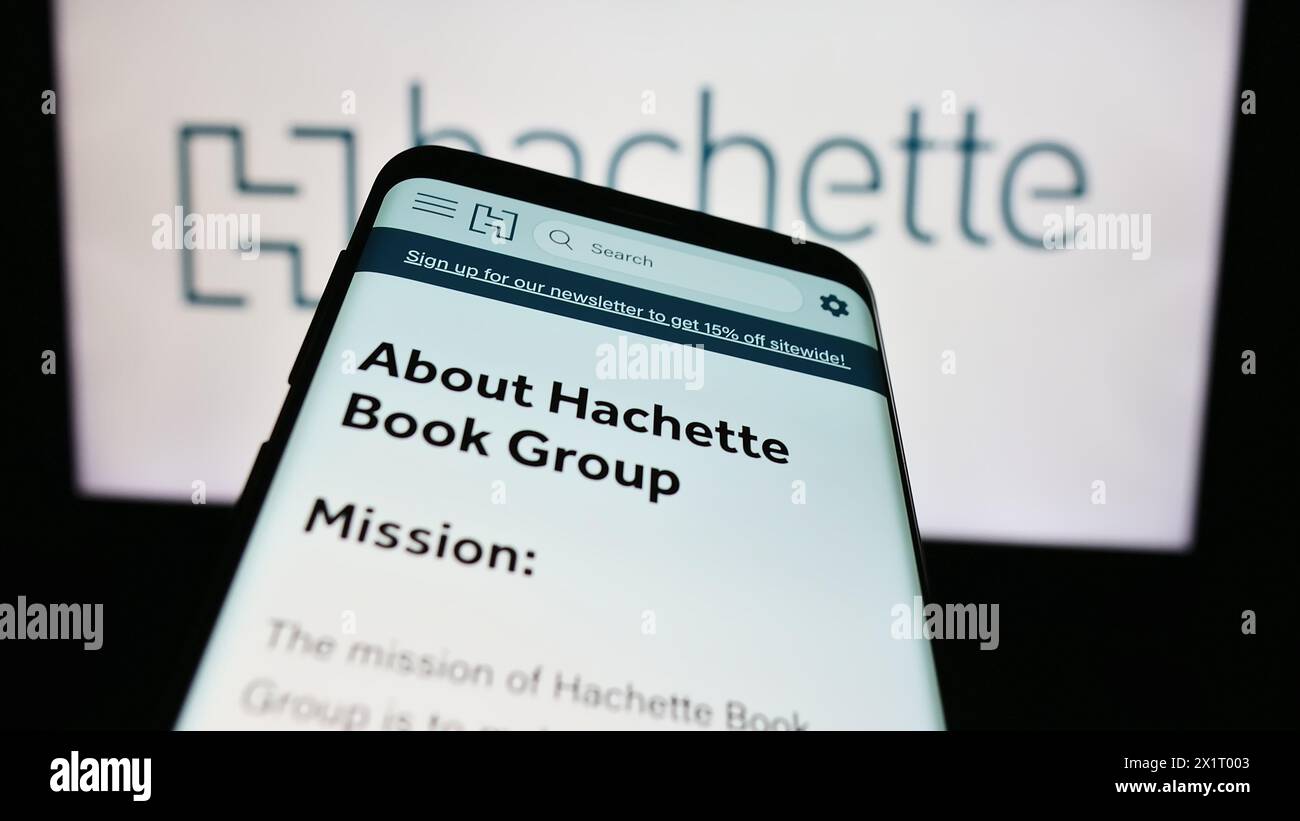 Telefono cellulare con sito web della casa editrice statunitense Hachette Book Group Inc (HBG) di fronte al logo aziendale. Mettere a fuoco in alto a sinistra sul display del telefono. Foto Stock