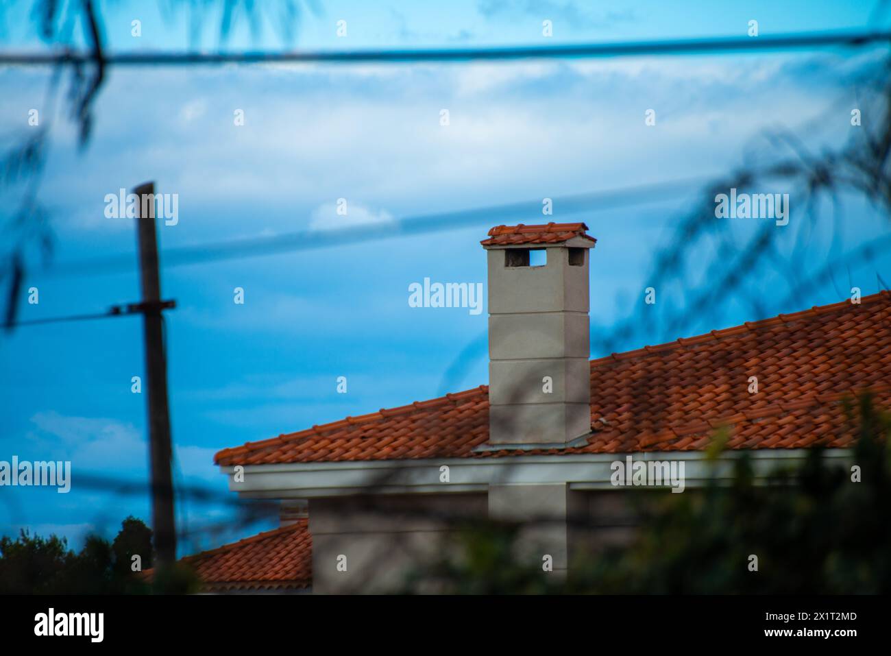 In mezzo a un clima nuvoloso, osserva l'emissione rovesciata dalla canna fumaria in cima al tetto, che si fonde con l'atmosfera tempestosa. Foto Stock
