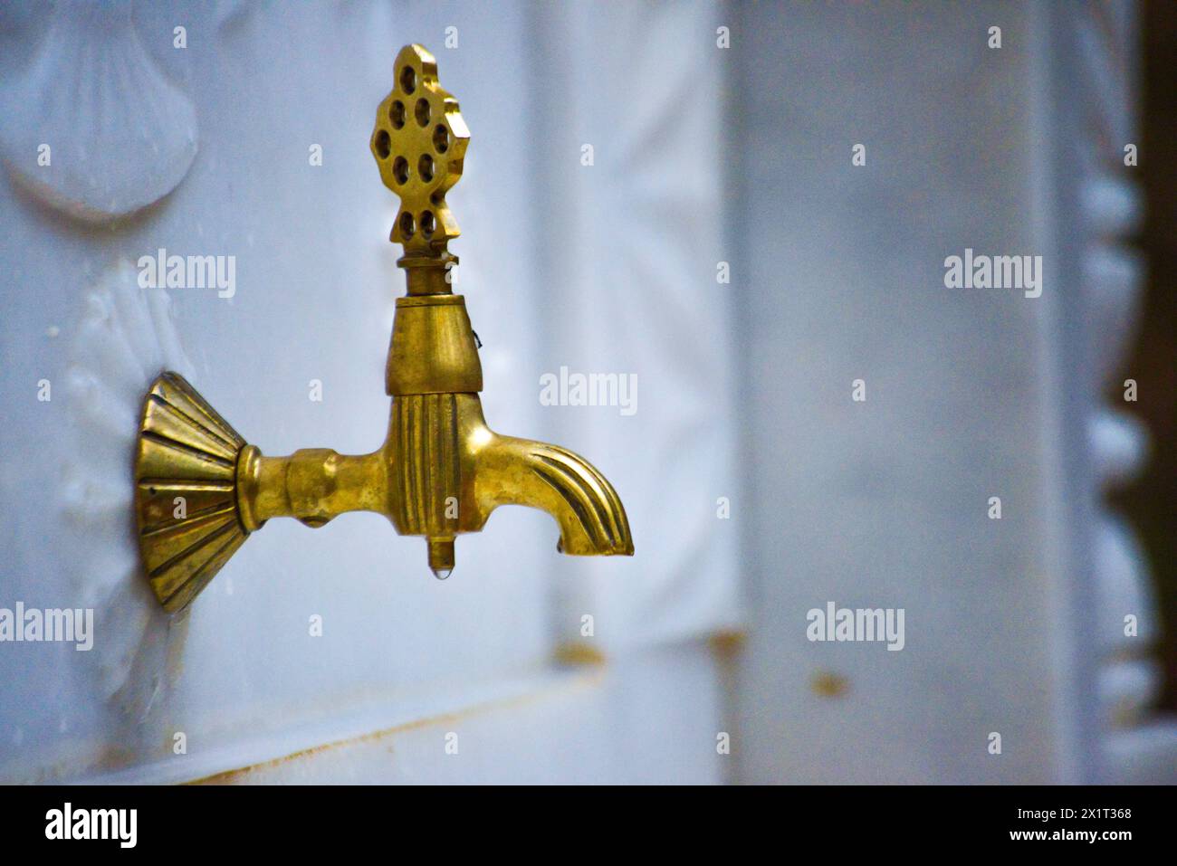 Un lussuoso rubinetto di fontana dorato adornato da intricati disegni in marmo bianco, che trasuda eleganza e opulenza. Foto Stock