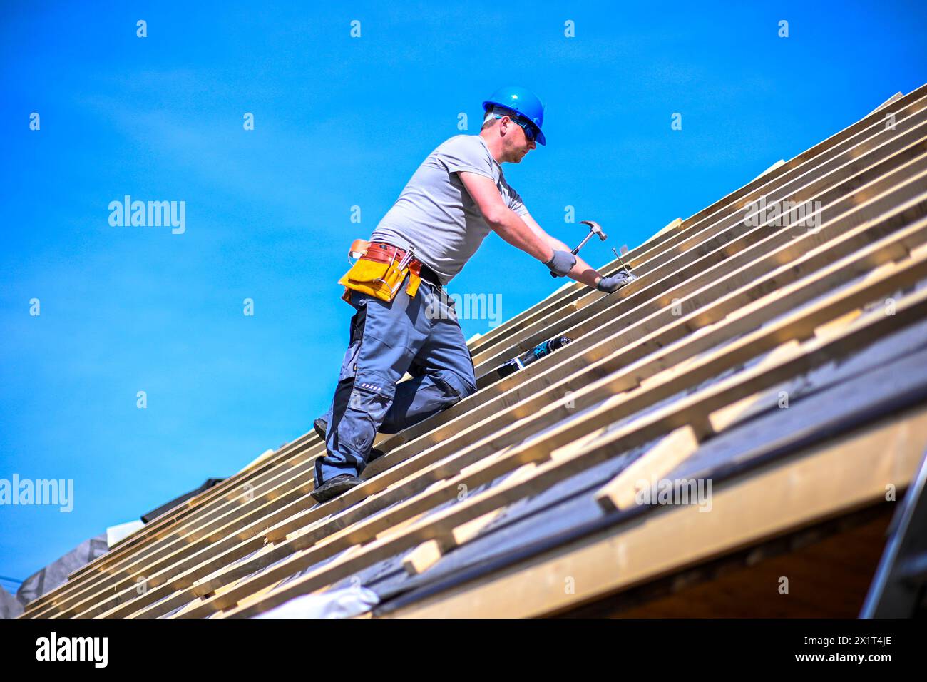 Riparazione e sostituzione del vecchio tetto con uno nuovo. Operaio edile con indumenti protettivi in piedi sul tetto con attrezzi. Foto Stock