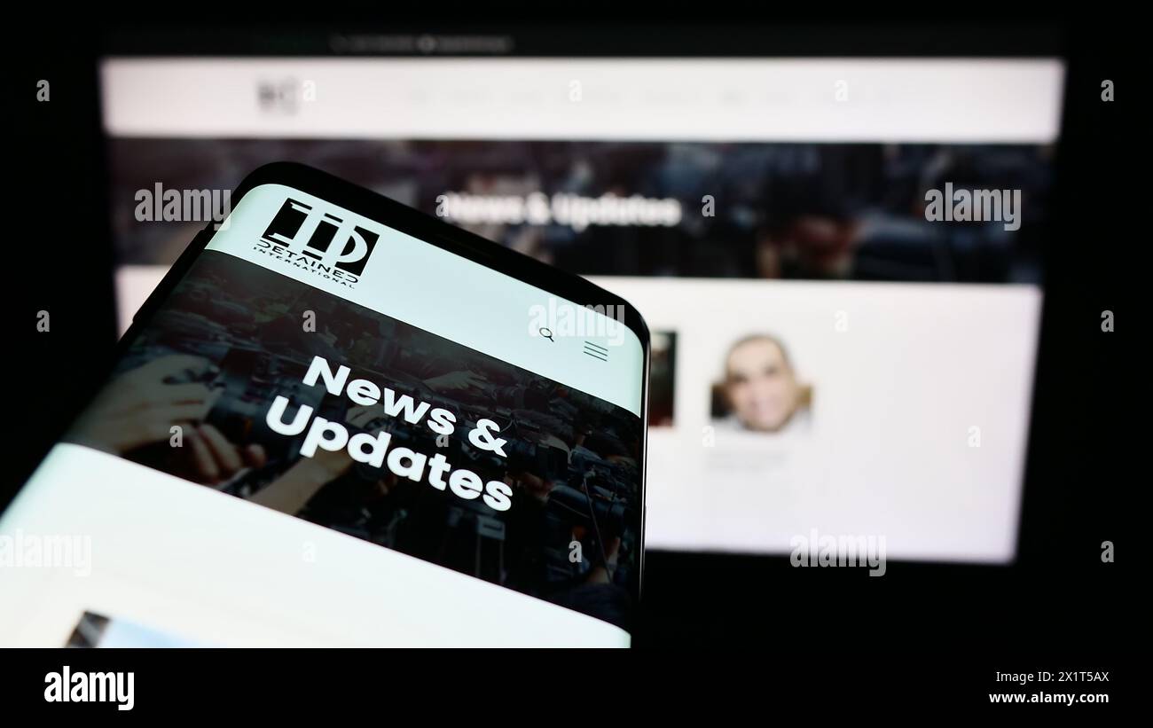 Smartphone con pagina Web e logo della ONG di difesa legale detenuti International davanti al monitor. Mettere a fuoco in alto a sinistra sul display del telefono. Foto Stock