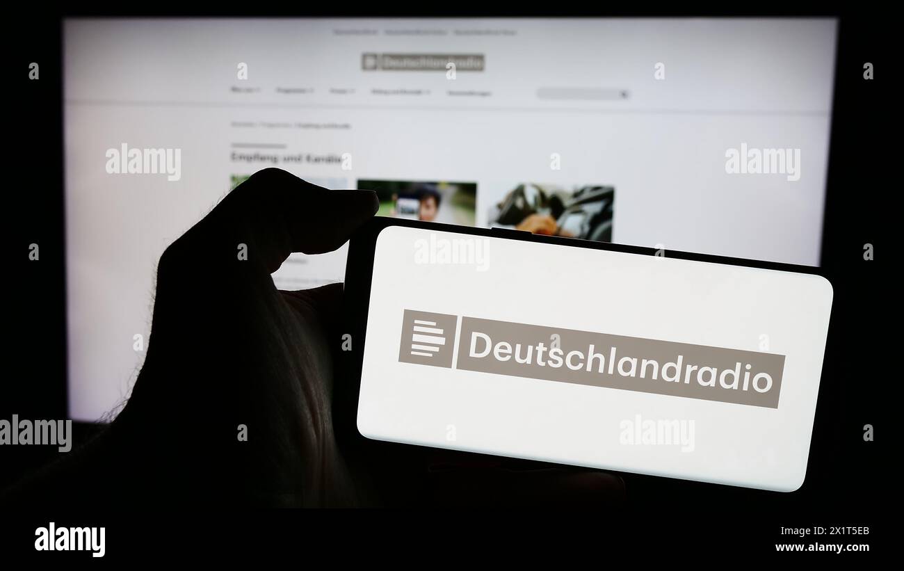 Persona che possiede un telefono cellulare con il logo dell'emittente radiofonica pubblica tedesca Deutschlandradio davanti alla pagina web. Mettere a fuoco il display del telefono. Foto Stock