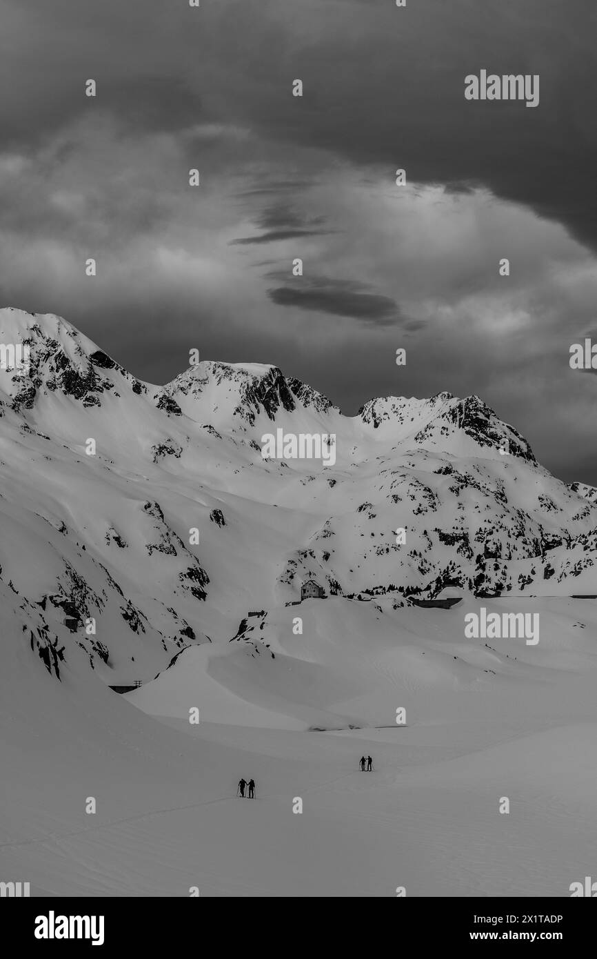 Atleti che praticano sci di fondo con un paesaggio di montagne innevate in una giornata di sole. Tramonto sulle montagne innevate. Foto Stock