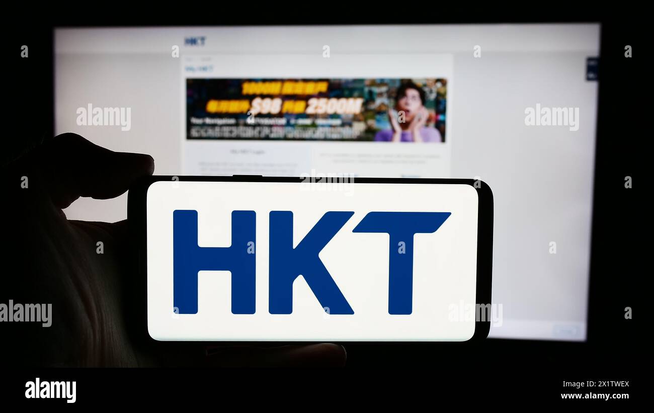 Persona che detiene un cellulare con il logo della società di telecomunicazioni HKT Limited (Hong Kong Telecom) di fronte alla pagina web. Mettere a fuoco il display del telefono. Foto Stock