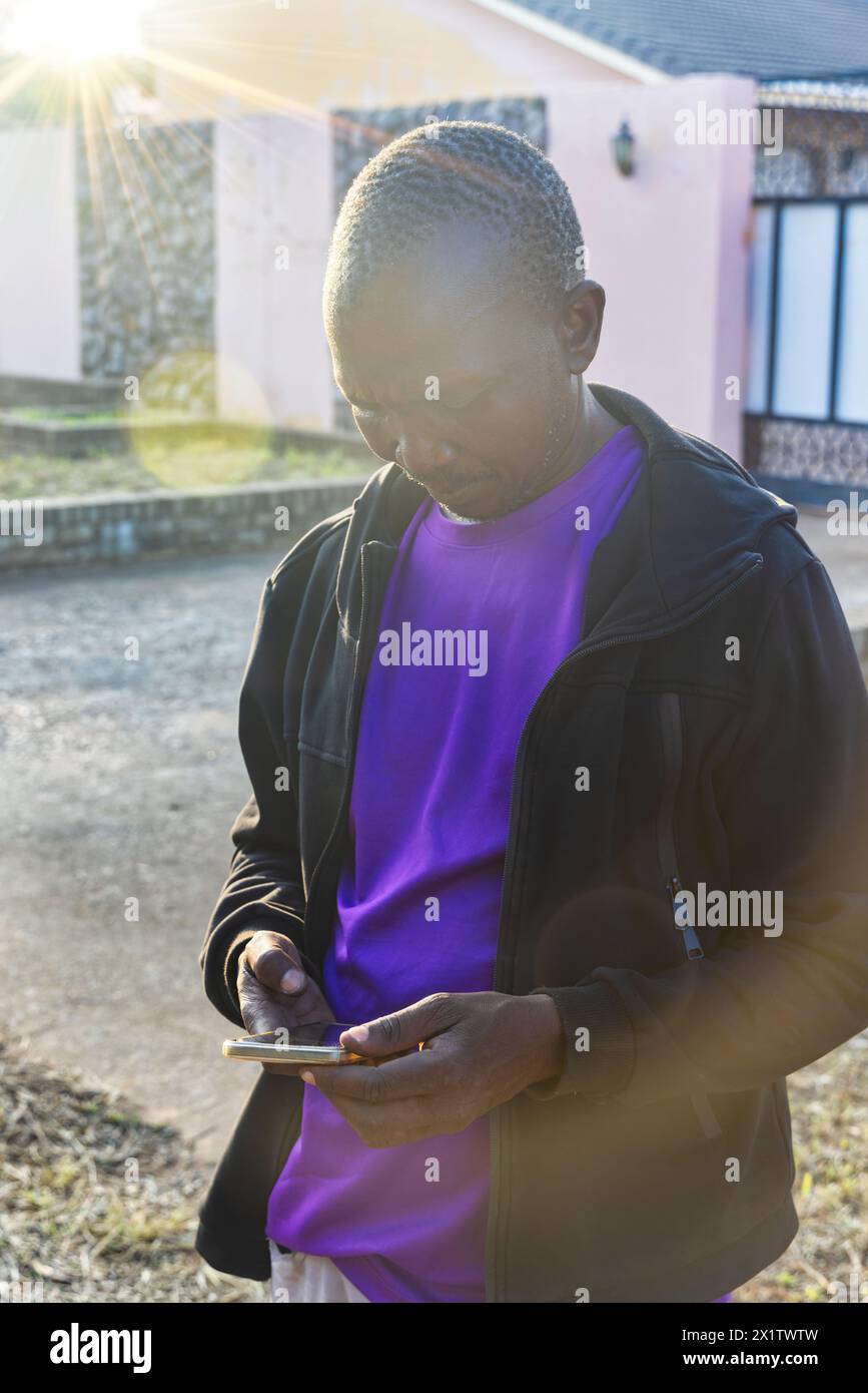 uomo africano medio adulto casual vestito con una felpa con cappuccio nera usando lo smartphone , all'aperto nel quartiere in una giornata di sole al tramonto Foto Stock