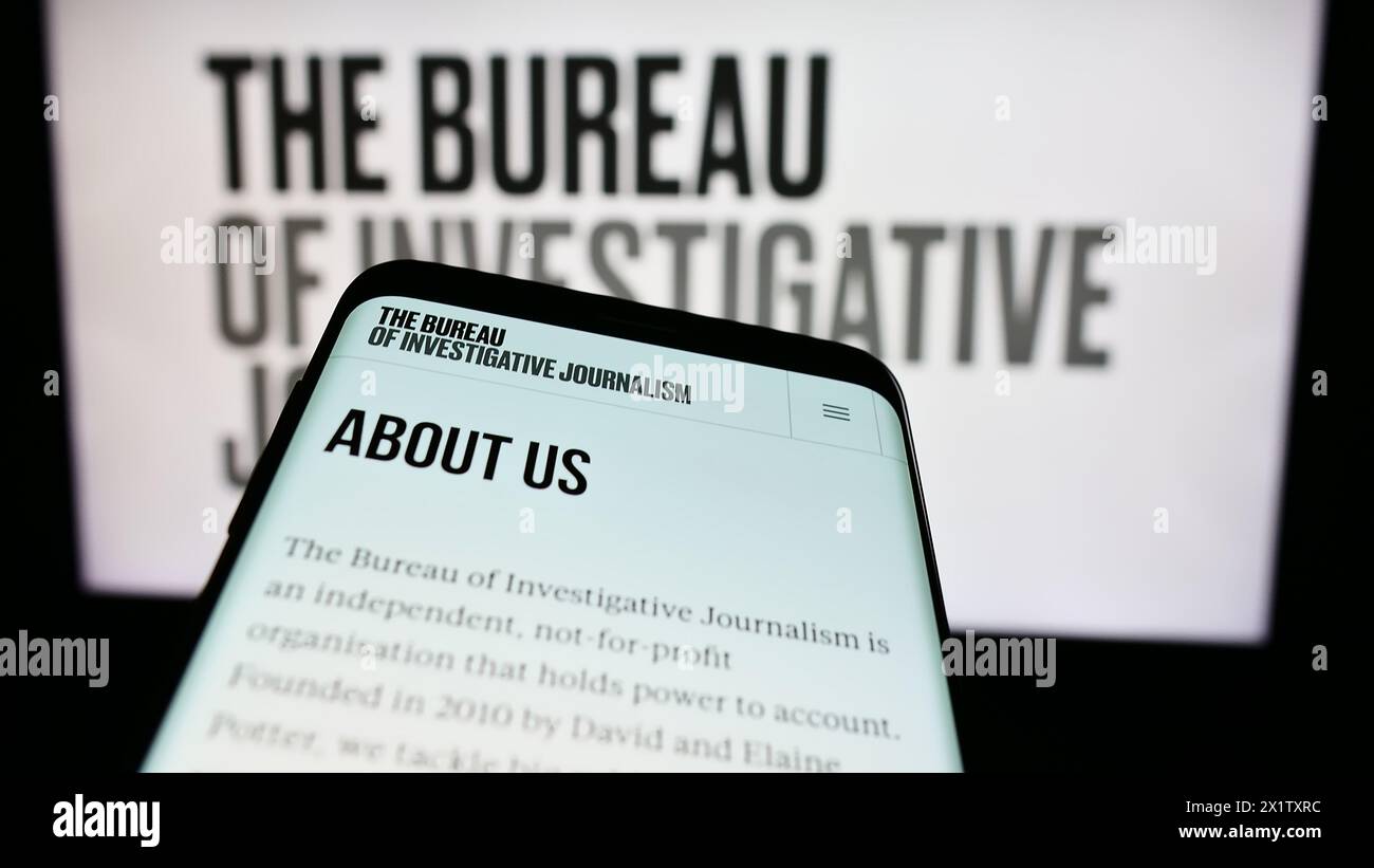Telefono cellulare con sito web dell'organizzazione il Bureau of Investigative Journalism (TBIJ) davanti al logo. Mettere a fuoco in alto a sinistra sul display del telefono. Foto Stock