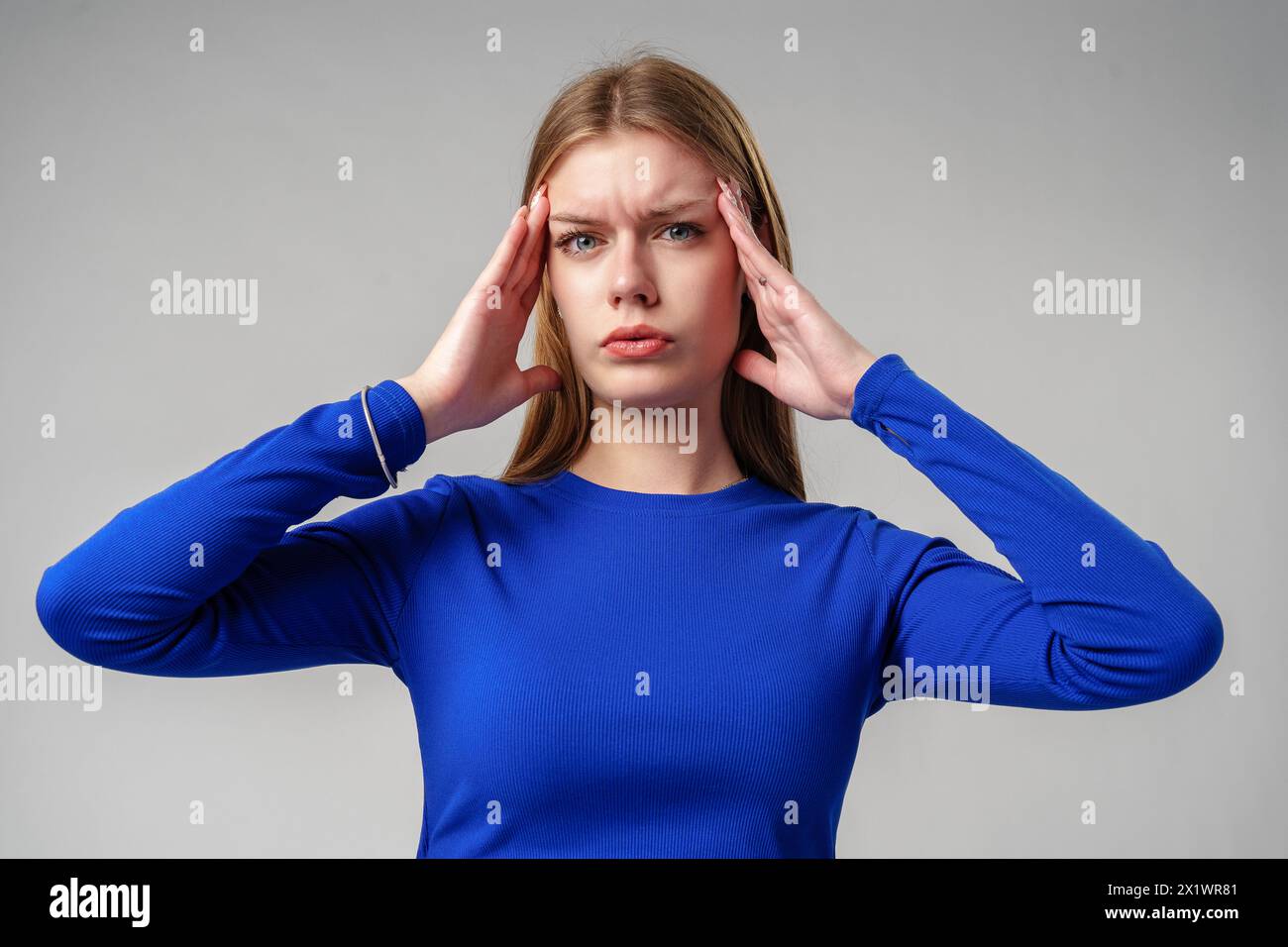 Donna in Blue Top che tiene le mani alle orecchie in studio Foto Stock