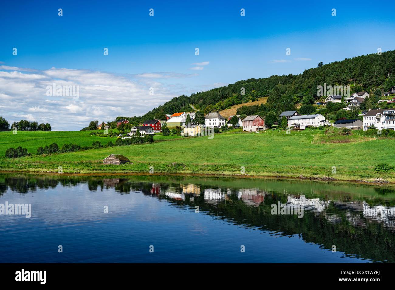 Tranquilla estate nel villaggio norvegese che si affaccia sul fiordo. Villaggio di Kvanne contro colline boscose, acque riflettenti dello Stangvikfjord norvegia Foto Stock