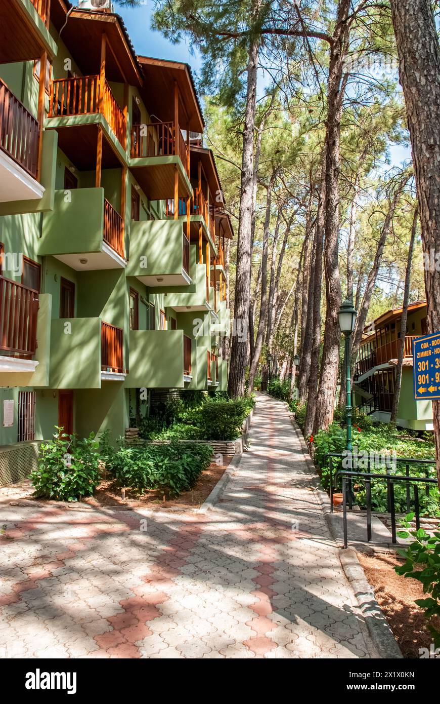 L'hotel, con facciate verdi e balconi in legno, si affaccia su una passerella pavimentata annidata tra pini nelle giornate di sole Foto Stock