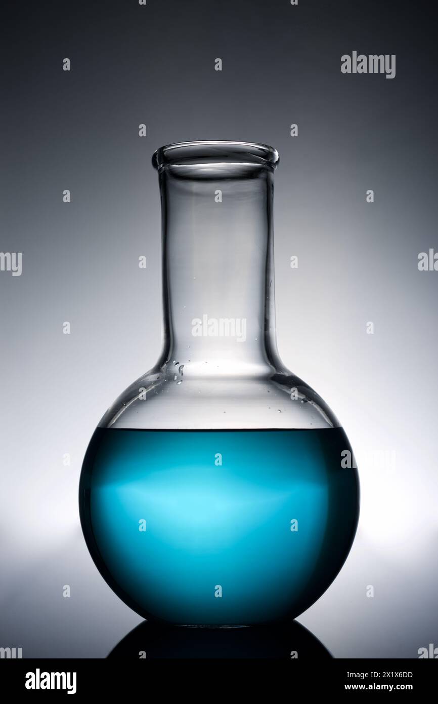 Primo piano di un becher in vetro con liquido blu posizionato su un piano di lavoro del laboratorio e retroilluminato. Foto Stock