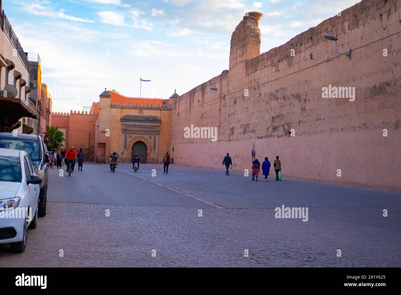 La gente cammina lungo l'alto muro della città Rossa di Marrakech affrettati a dedicarsi agli affari, all'autentico paesaggio urbano africano, alle attività quotidiane e alle interazioni che la gente vive Foto Stock