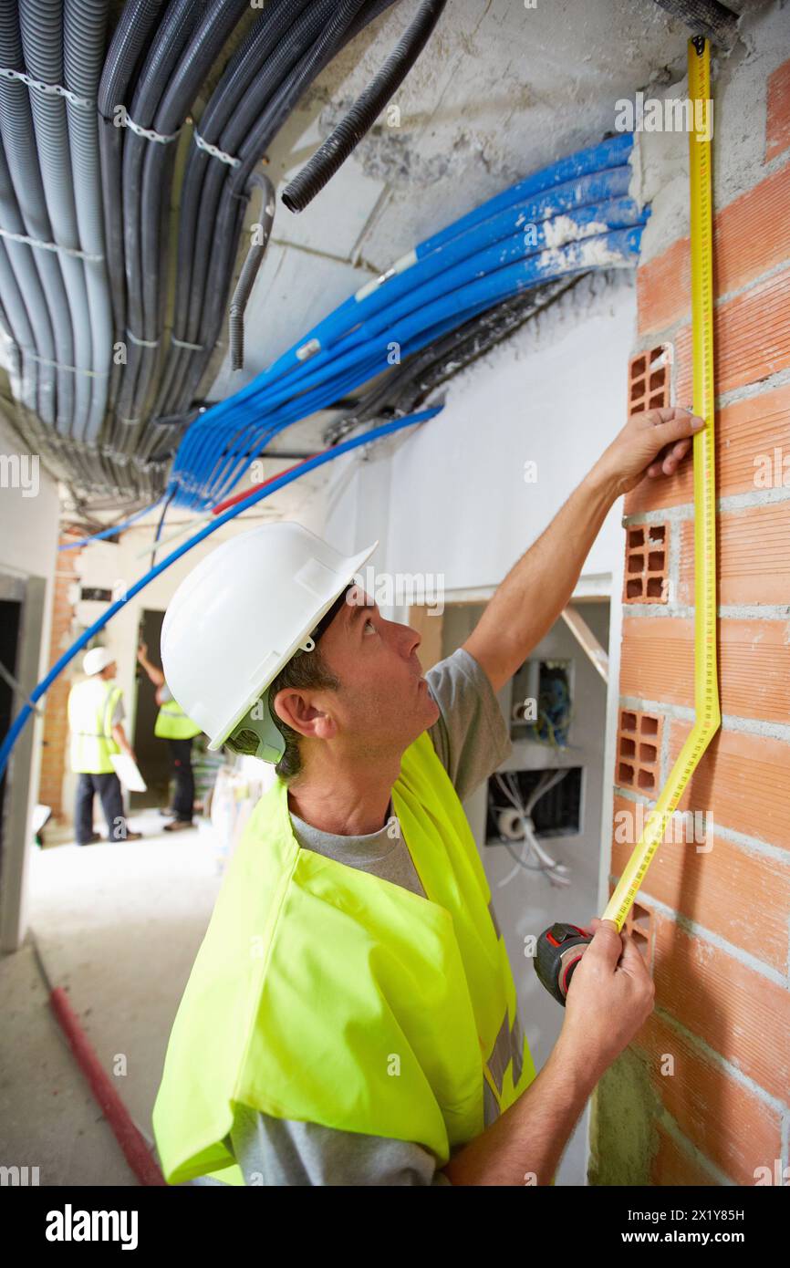 Lavoratore con dispositivi di protezione, DPI, presa di metro a nastro retrattile, costruzione di alloggi, pareti in mattoni, Paesi Baschi, Spagna. Foto Stock