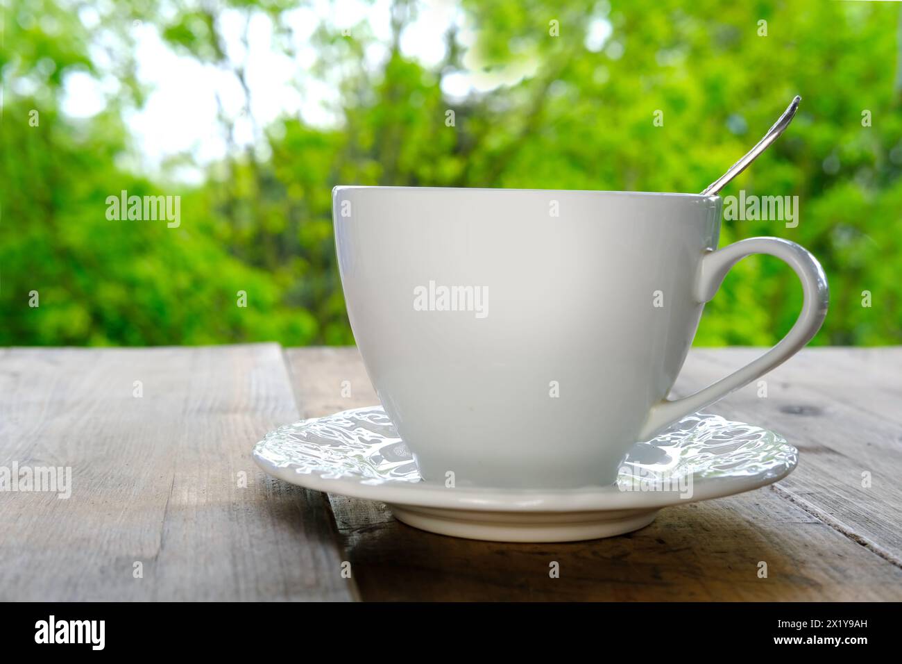 tazza bianca con caffè caldo e fragrante, tè, cappuccino su un tavolo di legno chiaro contro un verde giardino estivo, concetto di bere tè all'aperto, buona trama Foto Stock