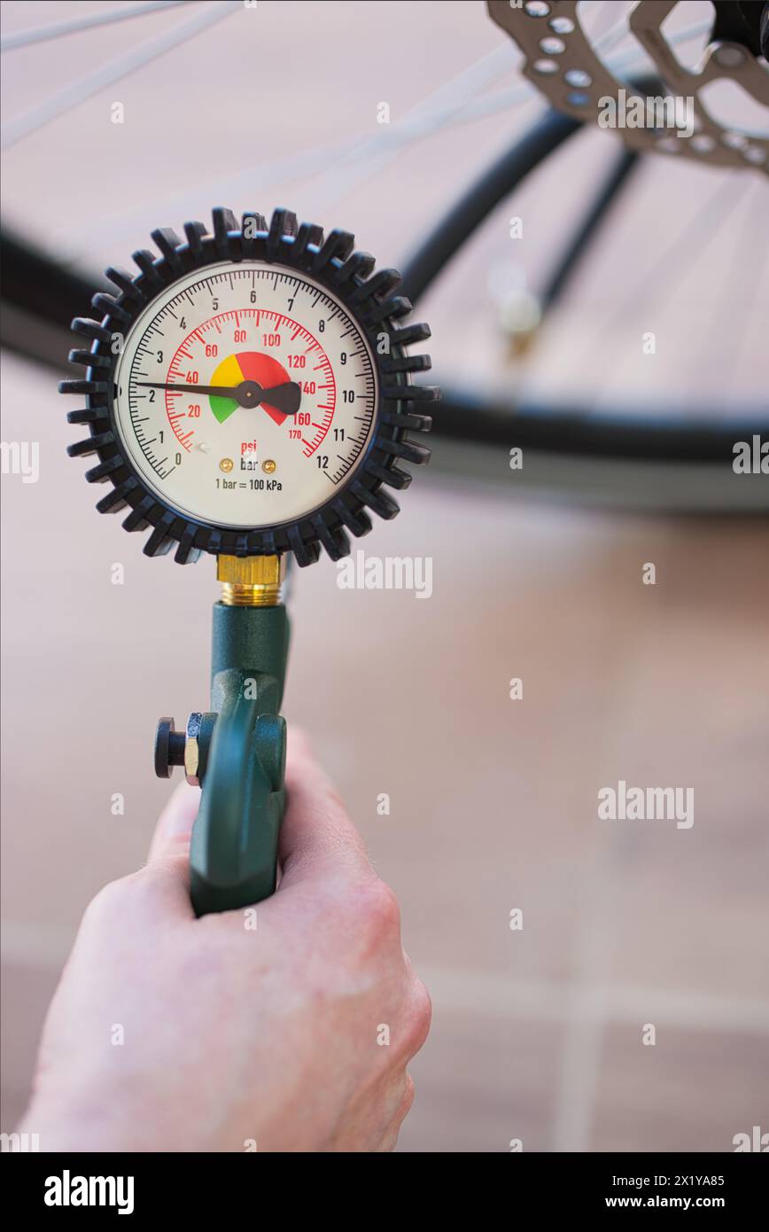 Tenere con la mano un manometro che indica 2,3 bar o 32 psi. Pneumatico per biciclette sfocato sullo sfondo. Contesto: Gonfiaggio degli pneumatici per biciclette, aria, monitoraggio Foto Stock