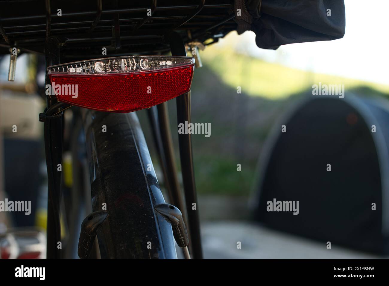 Vista ravvicinata di una luce di coda rossa e bianca montata su una bicicletta con portabagagli. Sullo sfondo, una tenda nera è sfocata. La scena sei tu Foto Stock