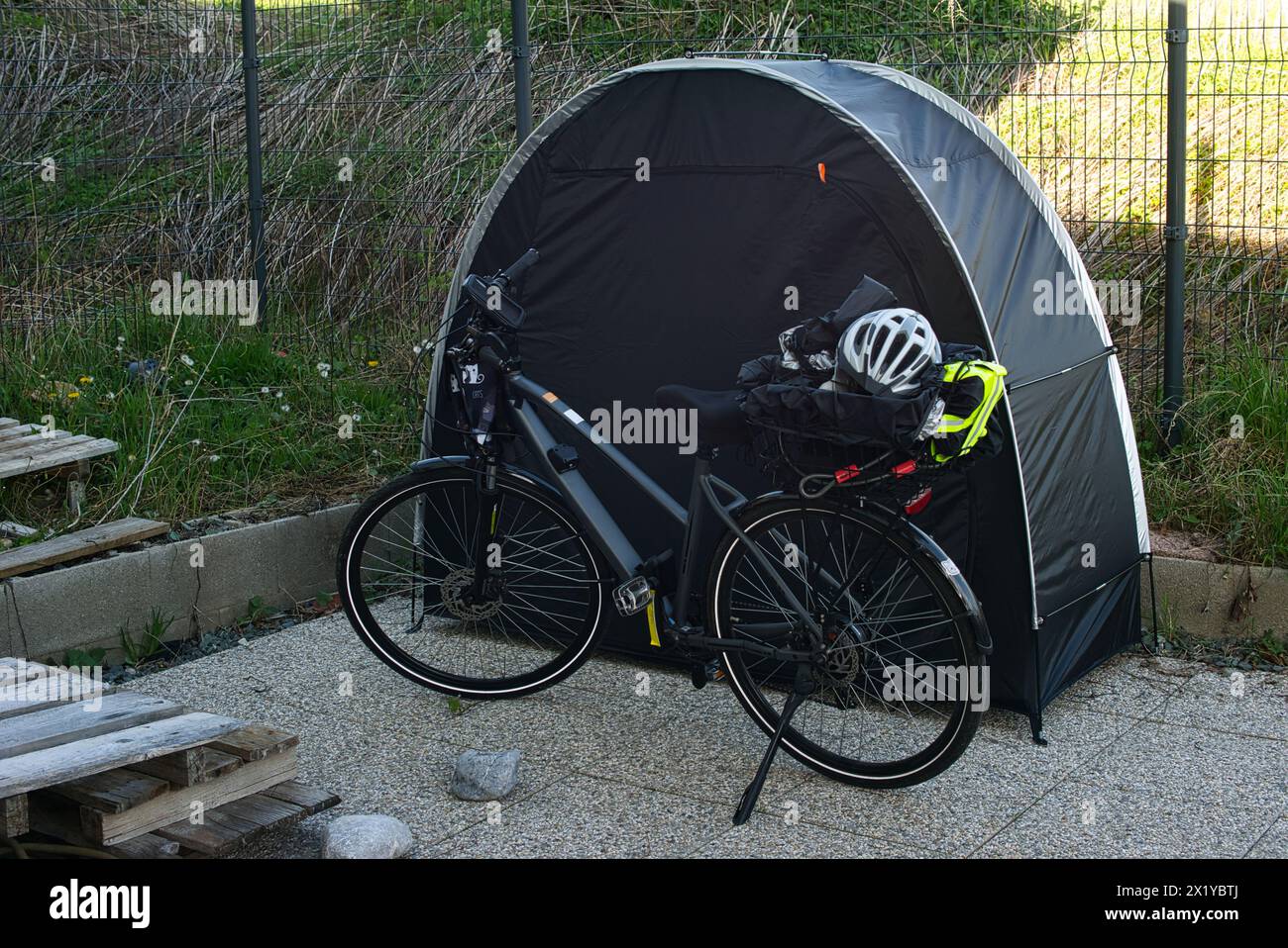 Bicicletta elettrica con portabagagli posizionato di fronte a una tenda per biciclette. Vari oggetti come un casco da bicicletta, giubbotto riflettente e copertura antipioggia Foto Stock