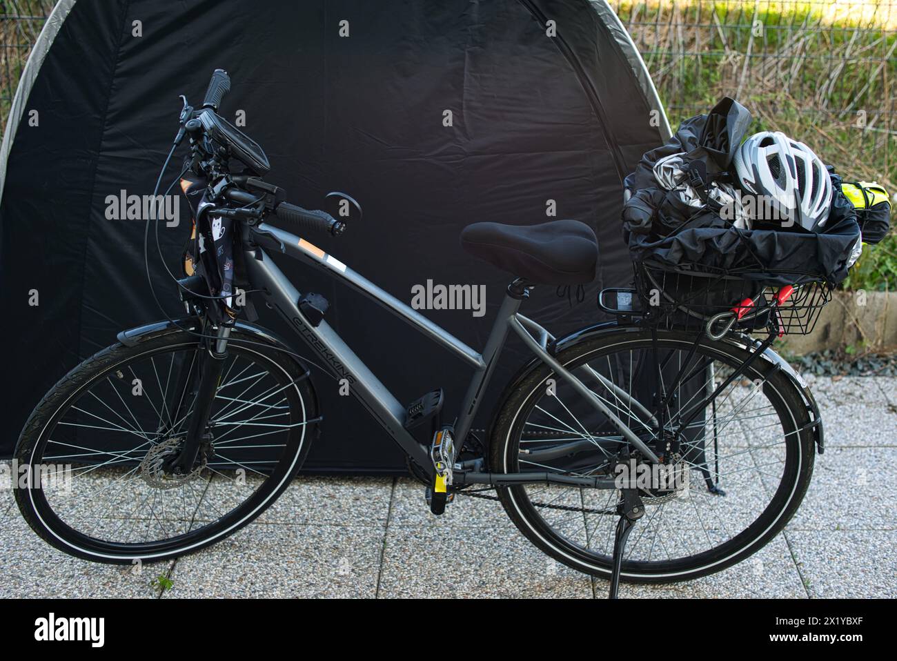 Bicicletta elettrica con portabagagli posizionato di fronte a una tenda per biciclette. Vari oggetti come un casco da bicicletta, giubbotto riflettente e copertura antipioggia Foto Stock