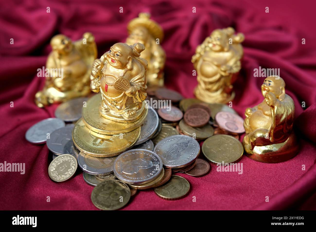 Scivolo di monete metalliche, valute di diversi paesi, bitcoin su un tendaggio rosso di lusso, cinque hotei giapponesi dio della ricchezza, simbolo di prosperità, co Foto Stock