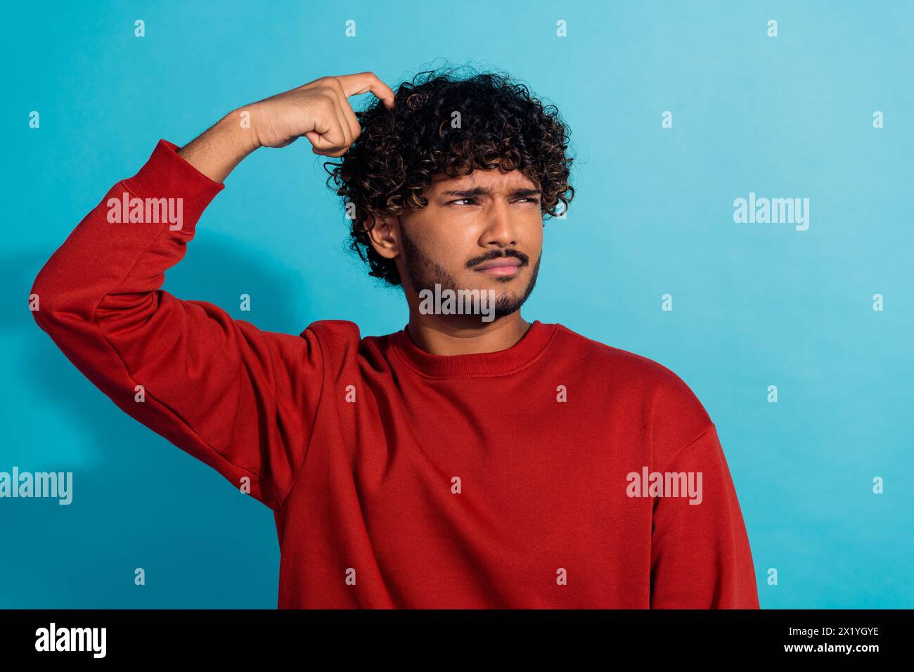Ritratto di un giovane uomo con un dito e una testa di graffio, interessato a uno spazio vuoto isolato su sfondo di colore blu Foto Stock
