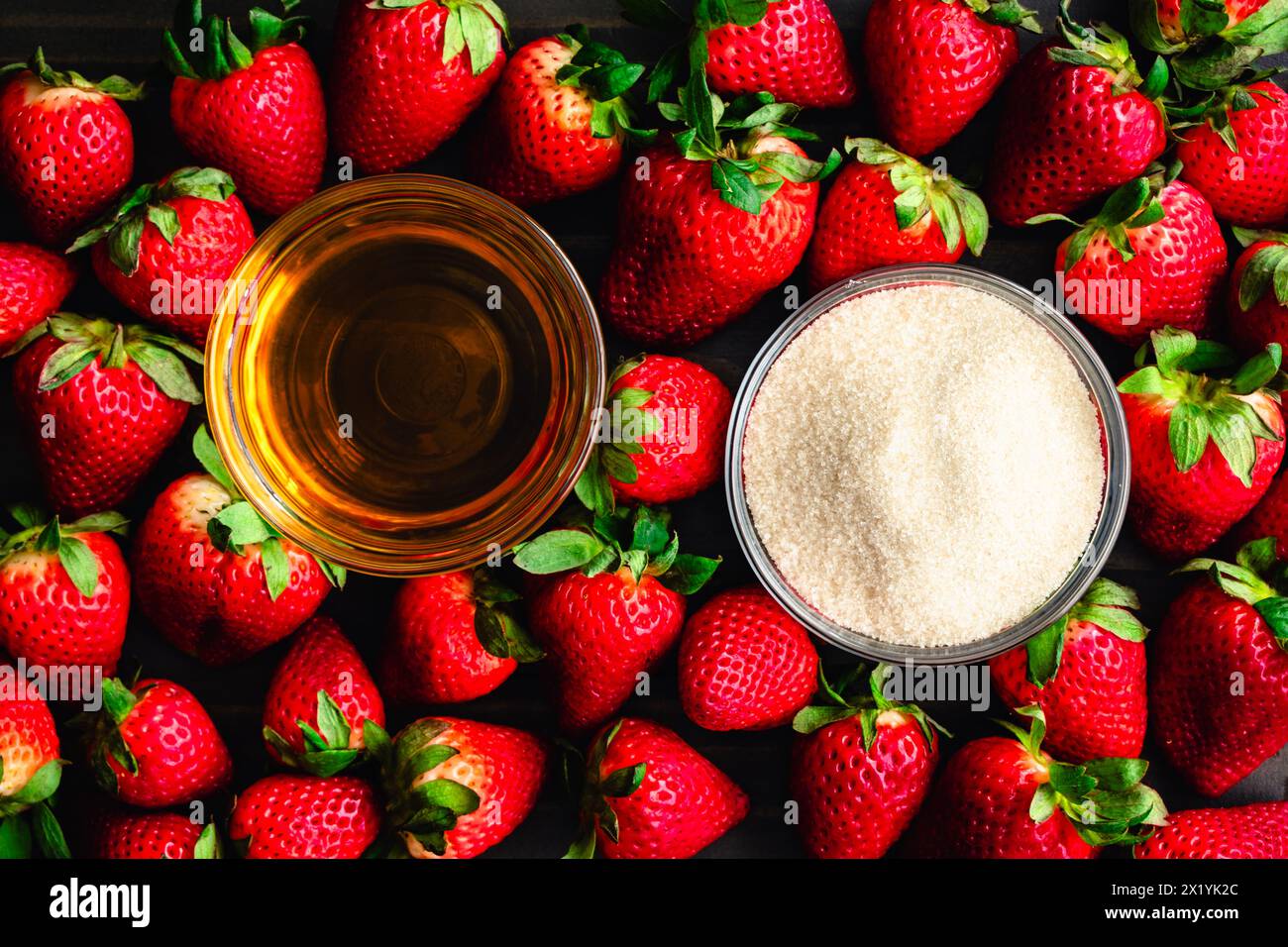 Strawberry Bourbon conserva ingredienti: Fragole fresche che circondano piatti di bourbon whiskey e zucchero di canna biologico visti direttamente dall'alto Foto Stock