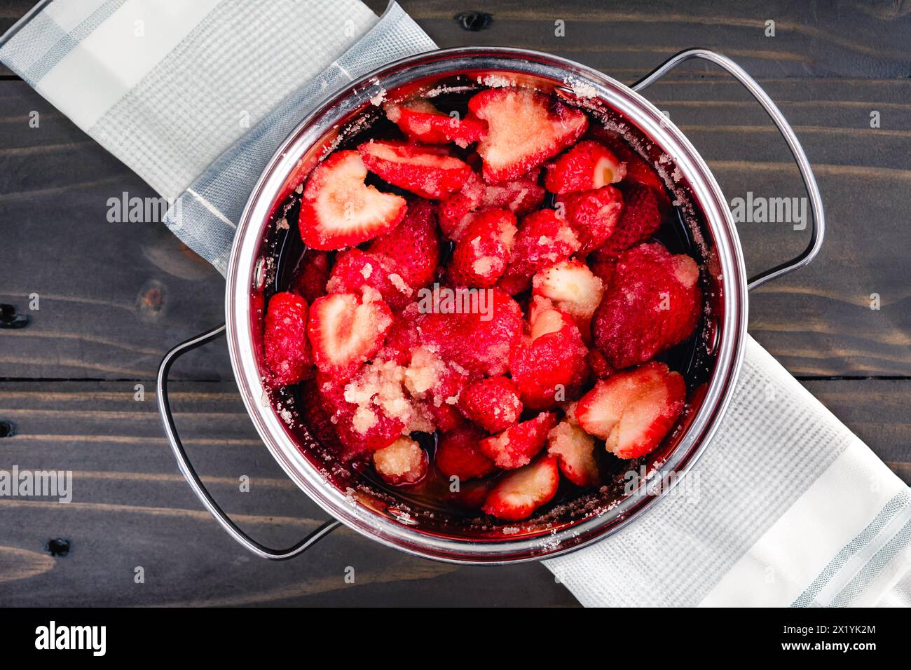 Fragole macerate in un piccolo forno olandese: Fette di fragole dopo la macerazione con zucchero di canna biologico in un cocotte Foto Stock