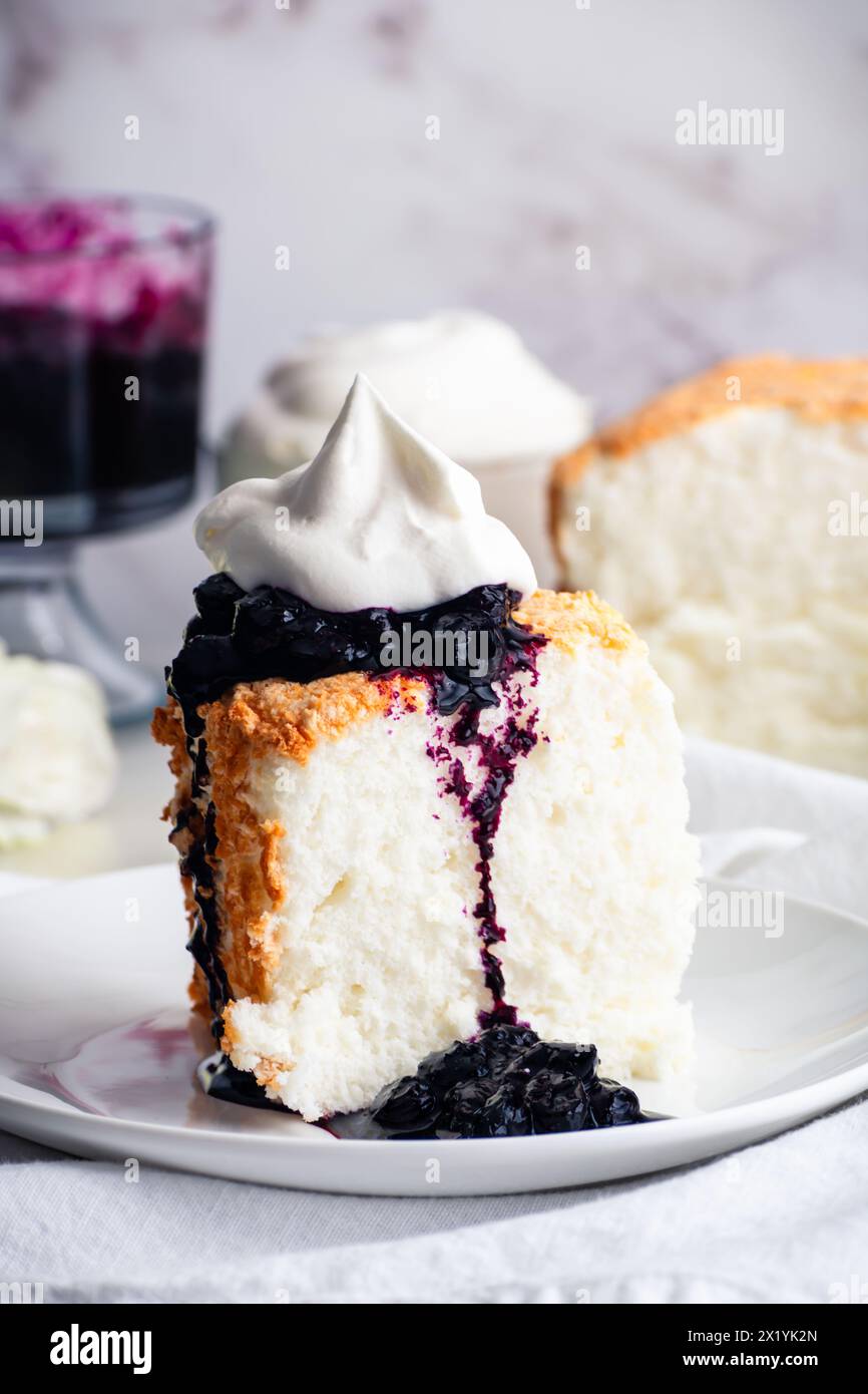 Torta Angel Food con salsa ai mirtilli e panna montata: Fetta di torta di pan di Spagna con marmellata di mirtilli e crema chantilly su un piatto Foto Stock