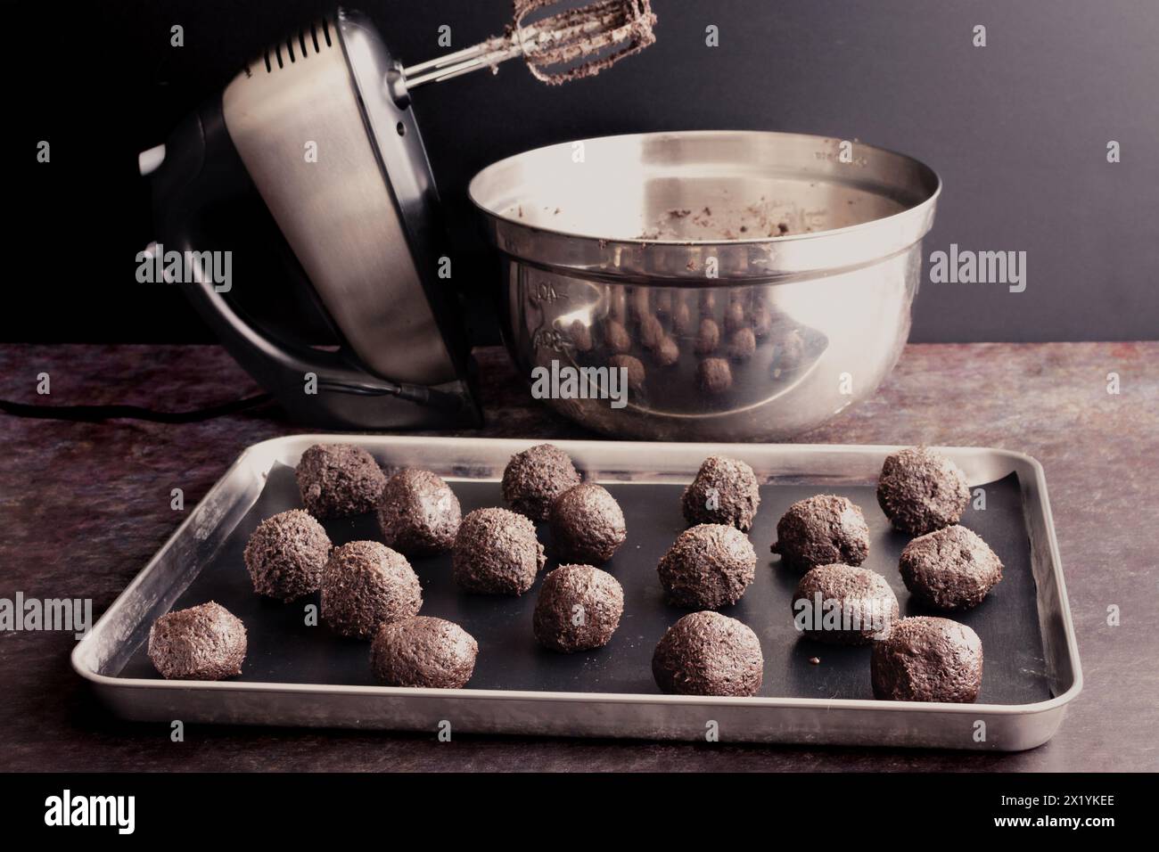 Biscotti non patinati e tartufi panna su una teglia: Ripieni di tartufo al formaggio cremoso di cioccolato con un mixer manuale e recipiente per mescolare sullo sfondo Foto Stock