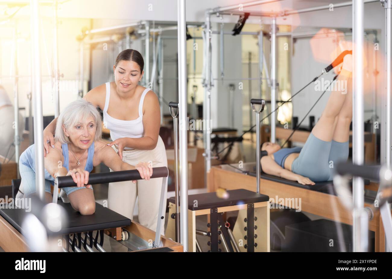 Donna anziana che fa pilates sul riformatore con una giovane addestratrice Foto Stock