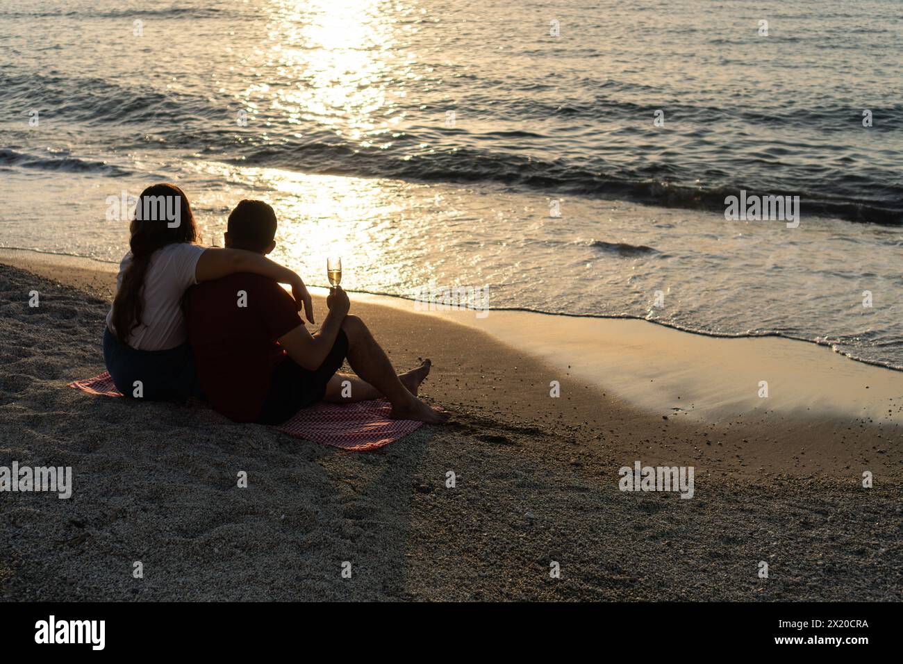 Una coppia gode di un tramonto con un bicchiere di vino in riva al mare calmante. Foto Stock