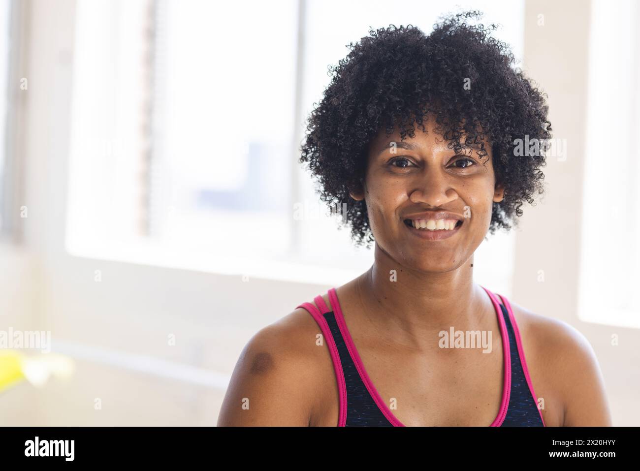 In una luminosa sala studio, donna birazziale con capelli neri ricci sorridenti alla macchina fotografica, copia spazio Foto Stock