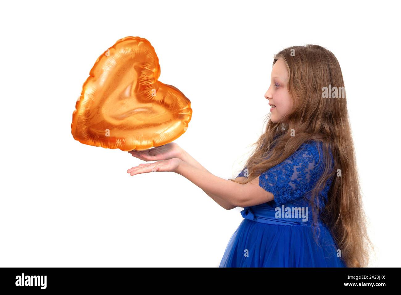 Una bambina con i capelli lunghi in un abito blu festoso regge un palloncino dorato a forma di cuore. Foto Stock